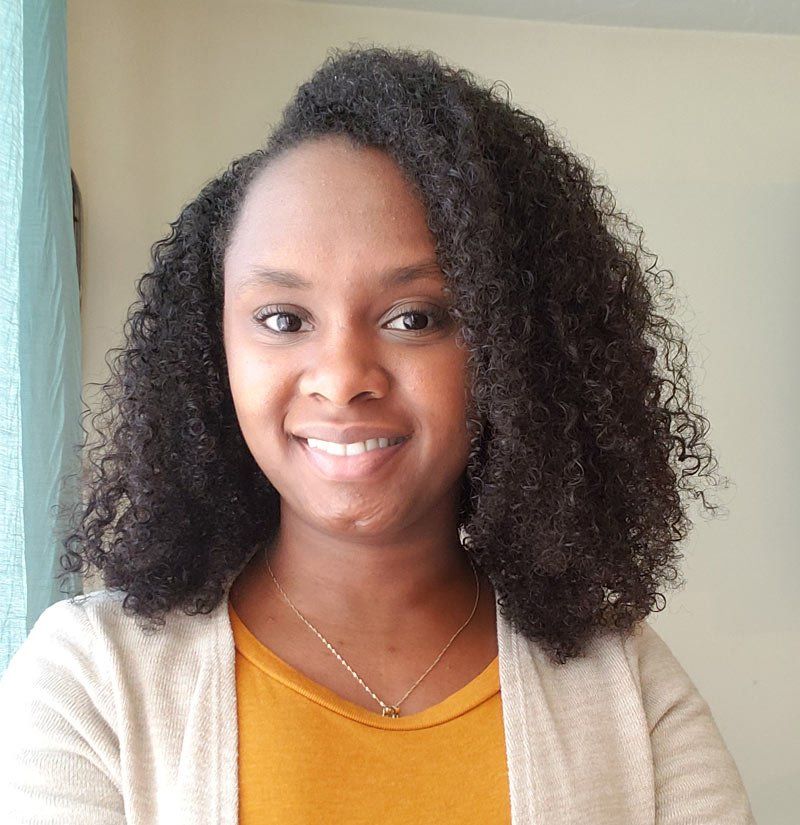 A woman with curly hair and a yellow shirt is smiling for the camera.