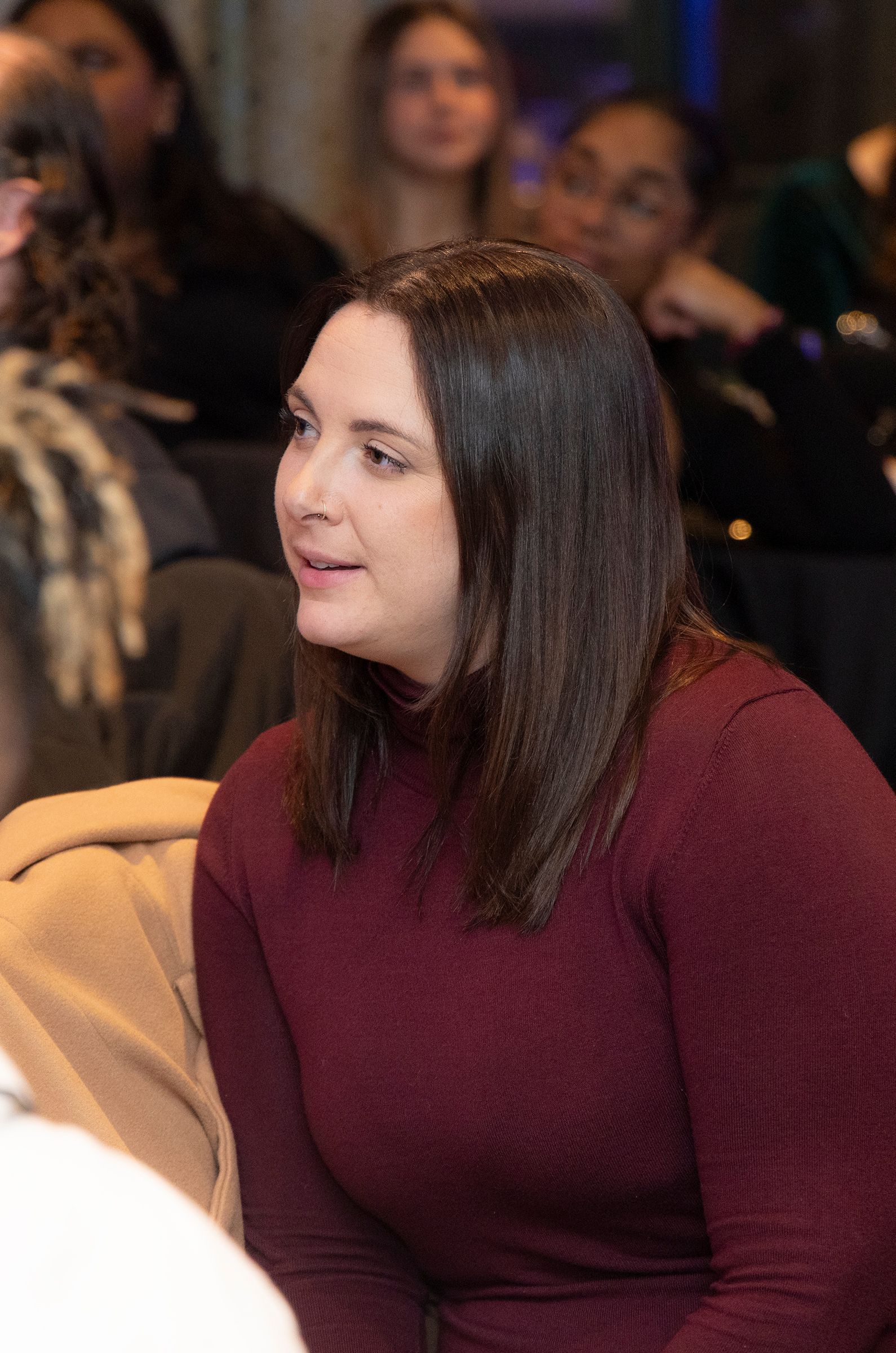 A woman in a maroon sweater is sitting in a crowd of people.