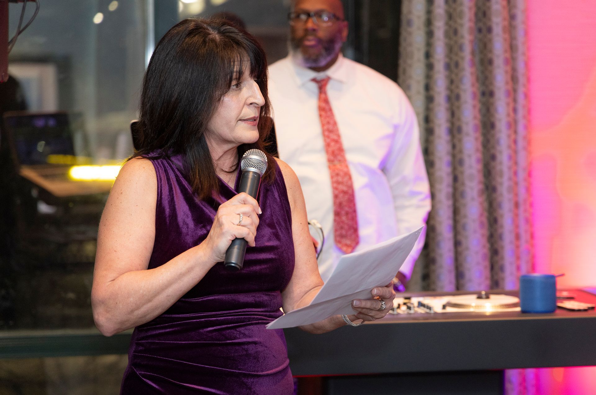 A woman in a purple dress is holding a microphone and giving a speech.