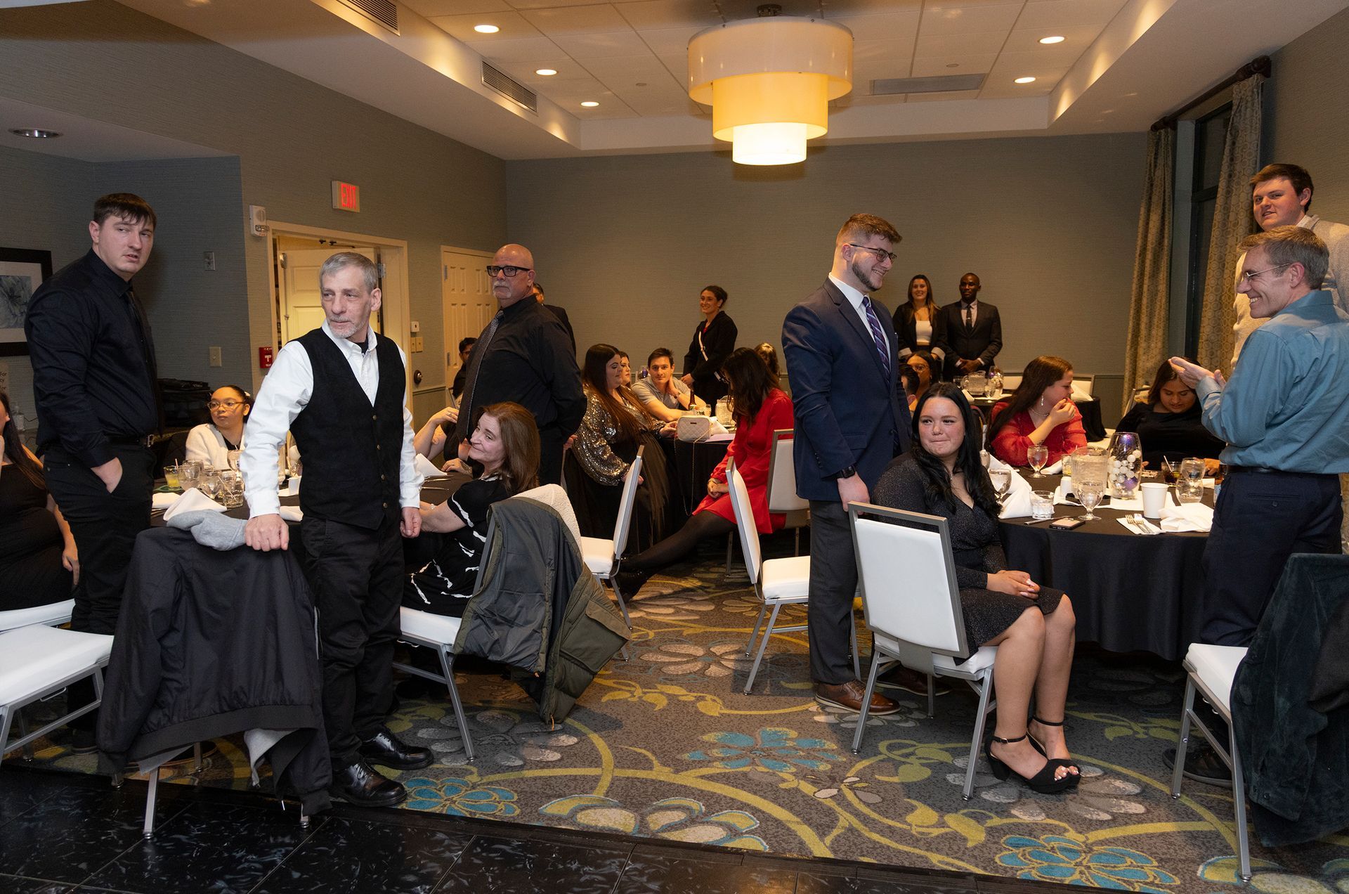 A group of people are standing in a room with tables and chairs.