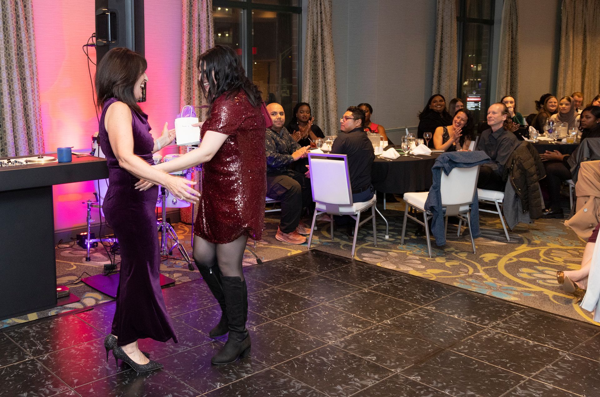 Two women are dancing on a dance floor in front of a crowd at a party.