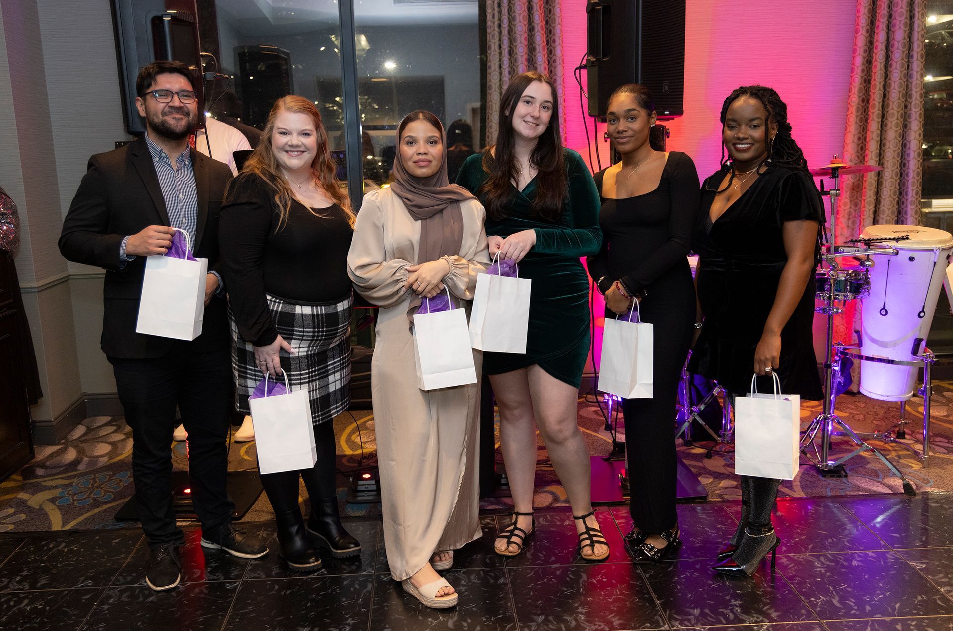 A group of people are standing next to each other in a room holding bags.