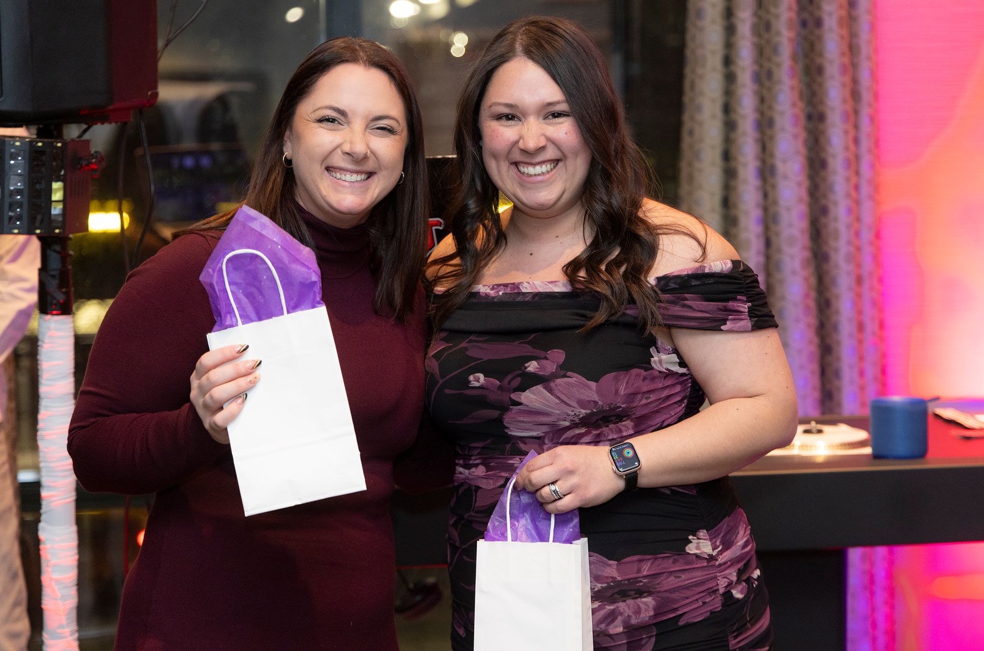 Two women are posing for a picture while holding purple bags.