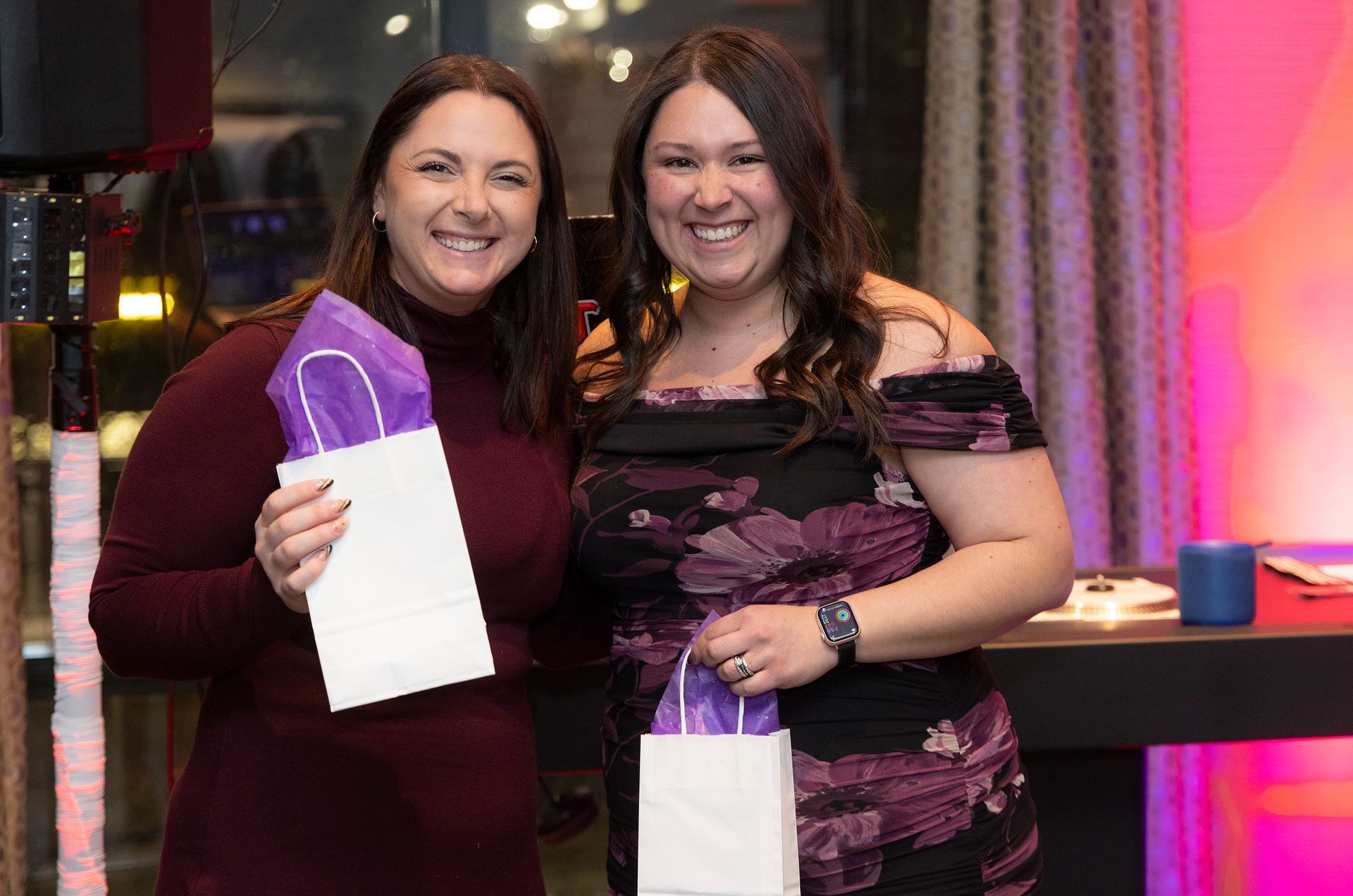Two women are posing for a picture while holding purple bags.