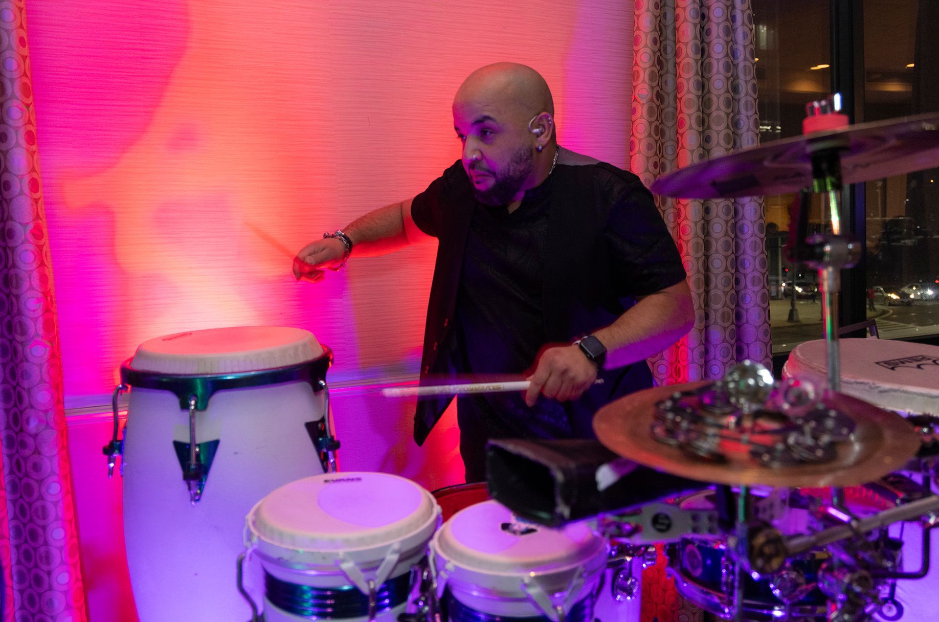 A man is playing drums in front of a pink wall.