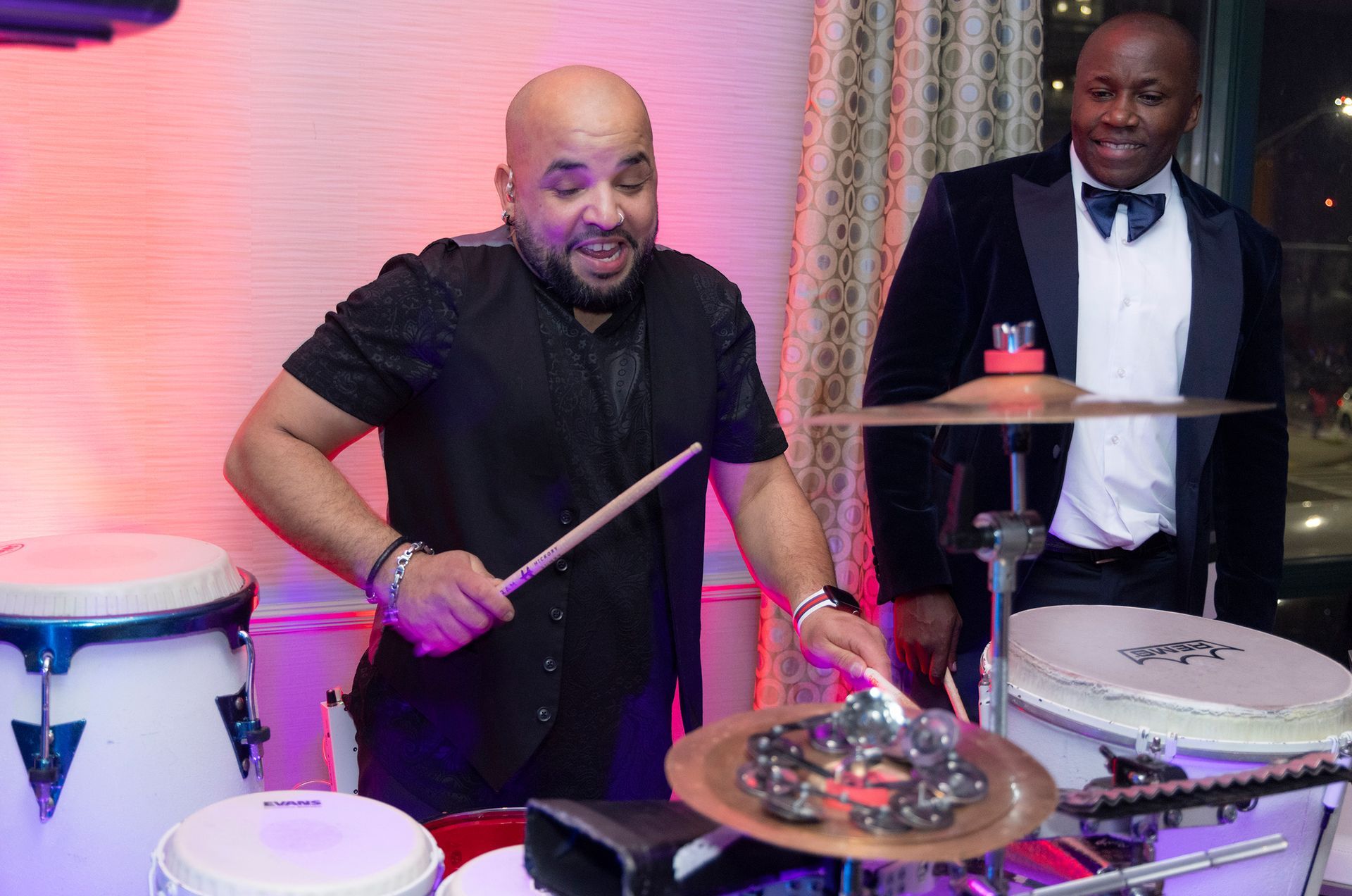 Two men are playing drums in a room.