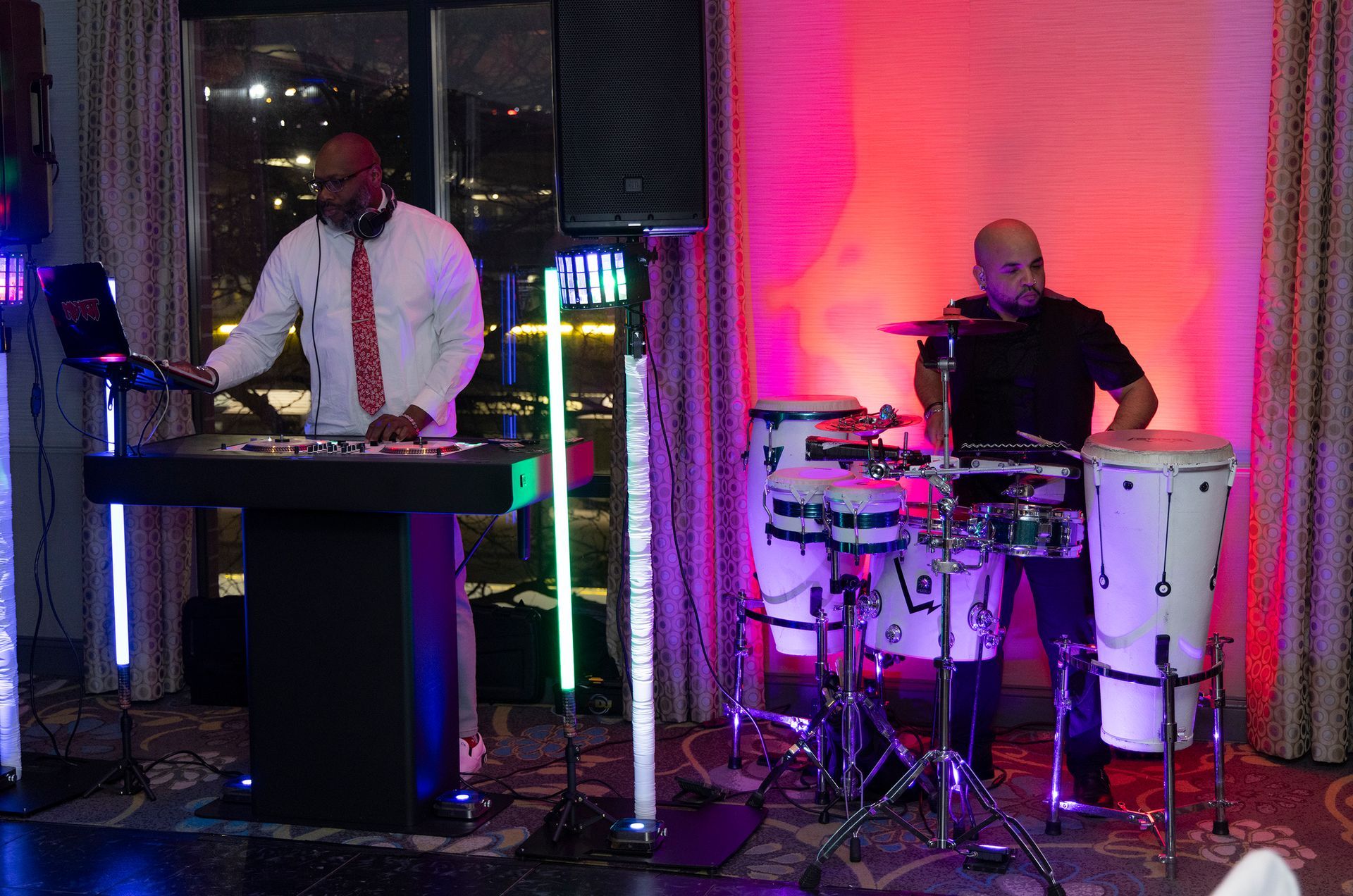 A dj and a drummer are playing drums in a room.