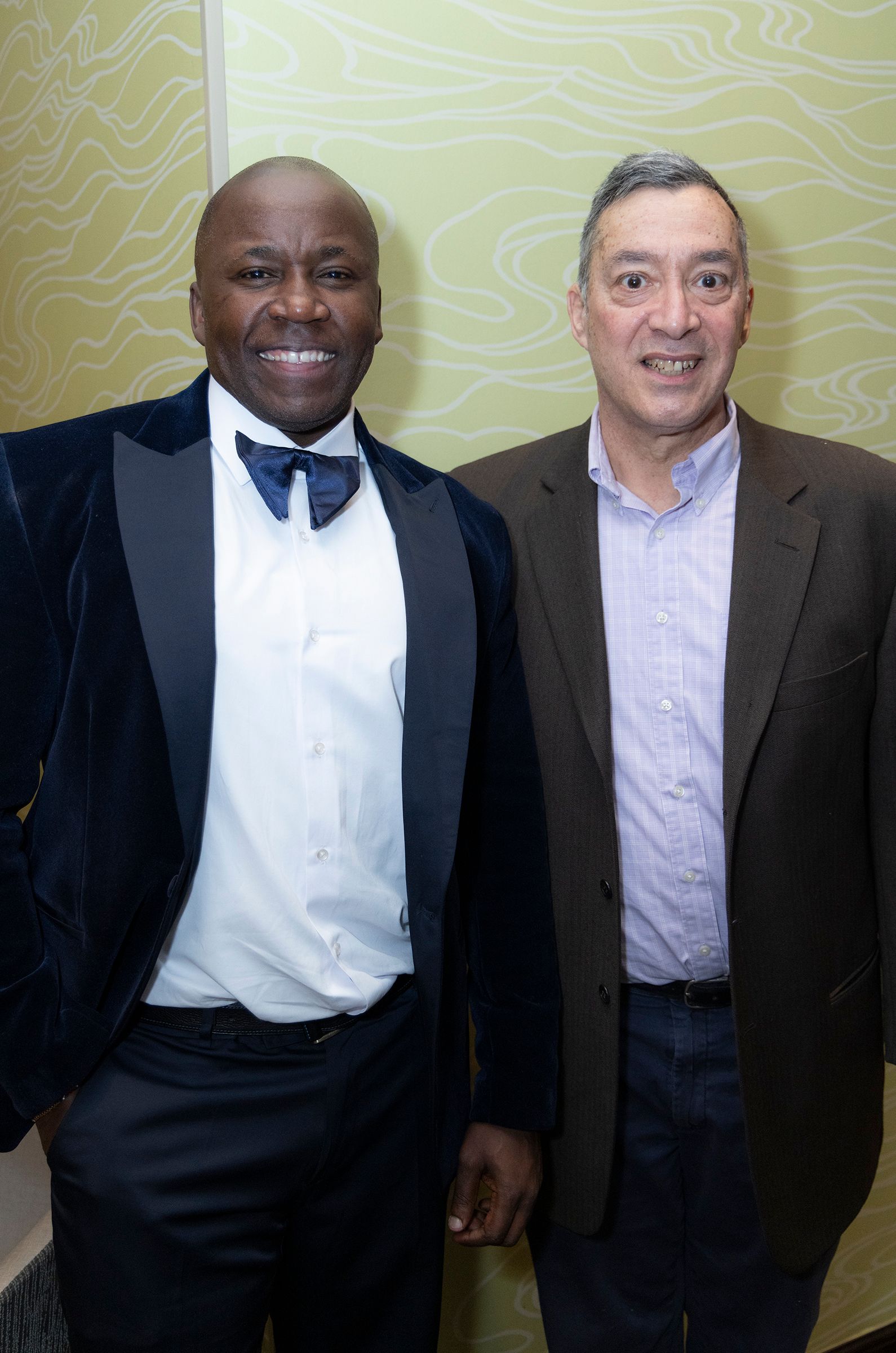 Two men in suits and bow ties are posing for a picture.