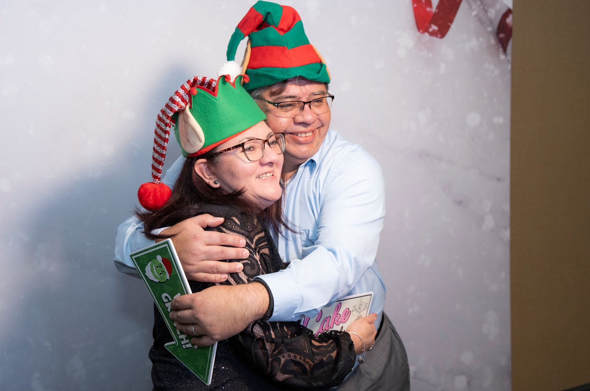 A man and a woman wearing elf hats are hugging each other.