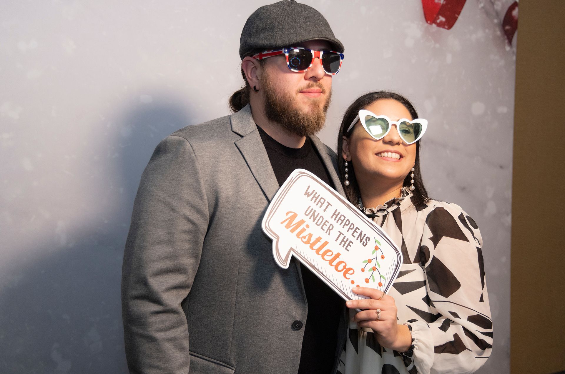 A man and a woman are posing for a picture while holding a sign that says mistletoe.