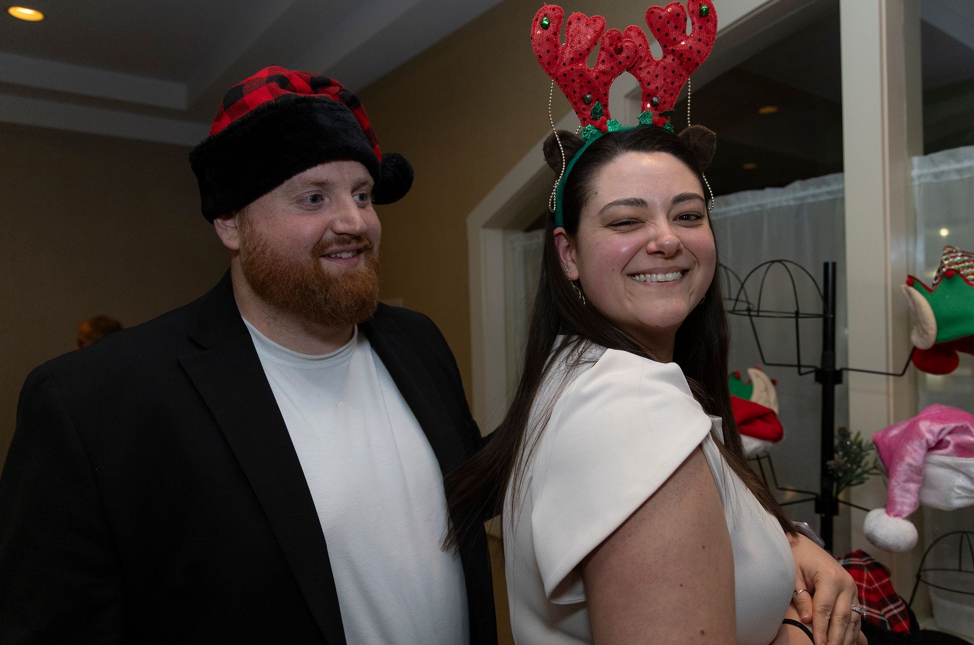 A man and a woman are standing next to each other wearing christmas hats.