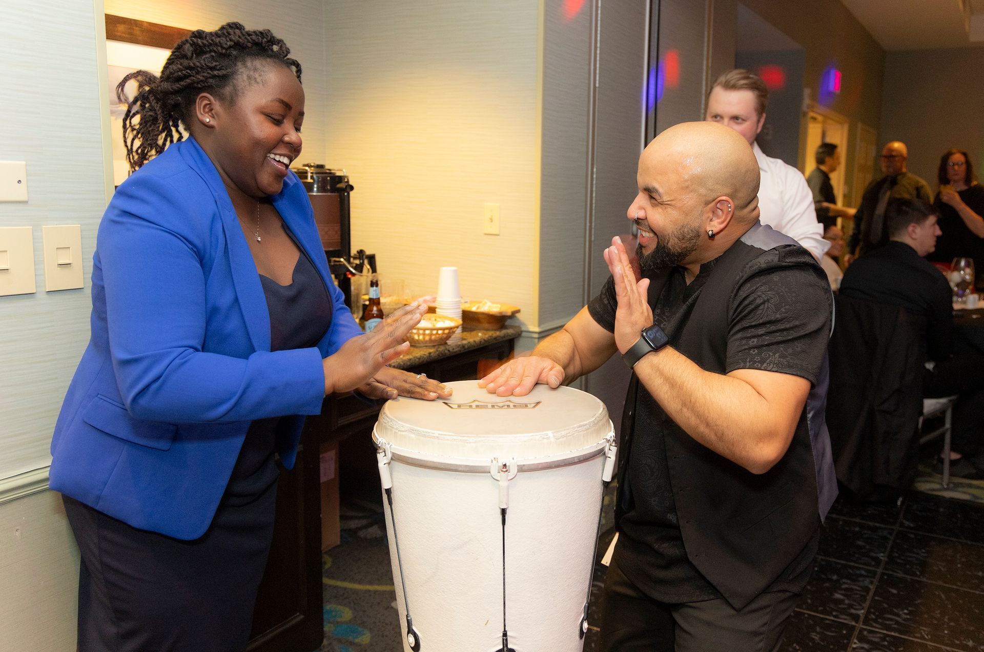 A man and a woman are playing a drum in a room.