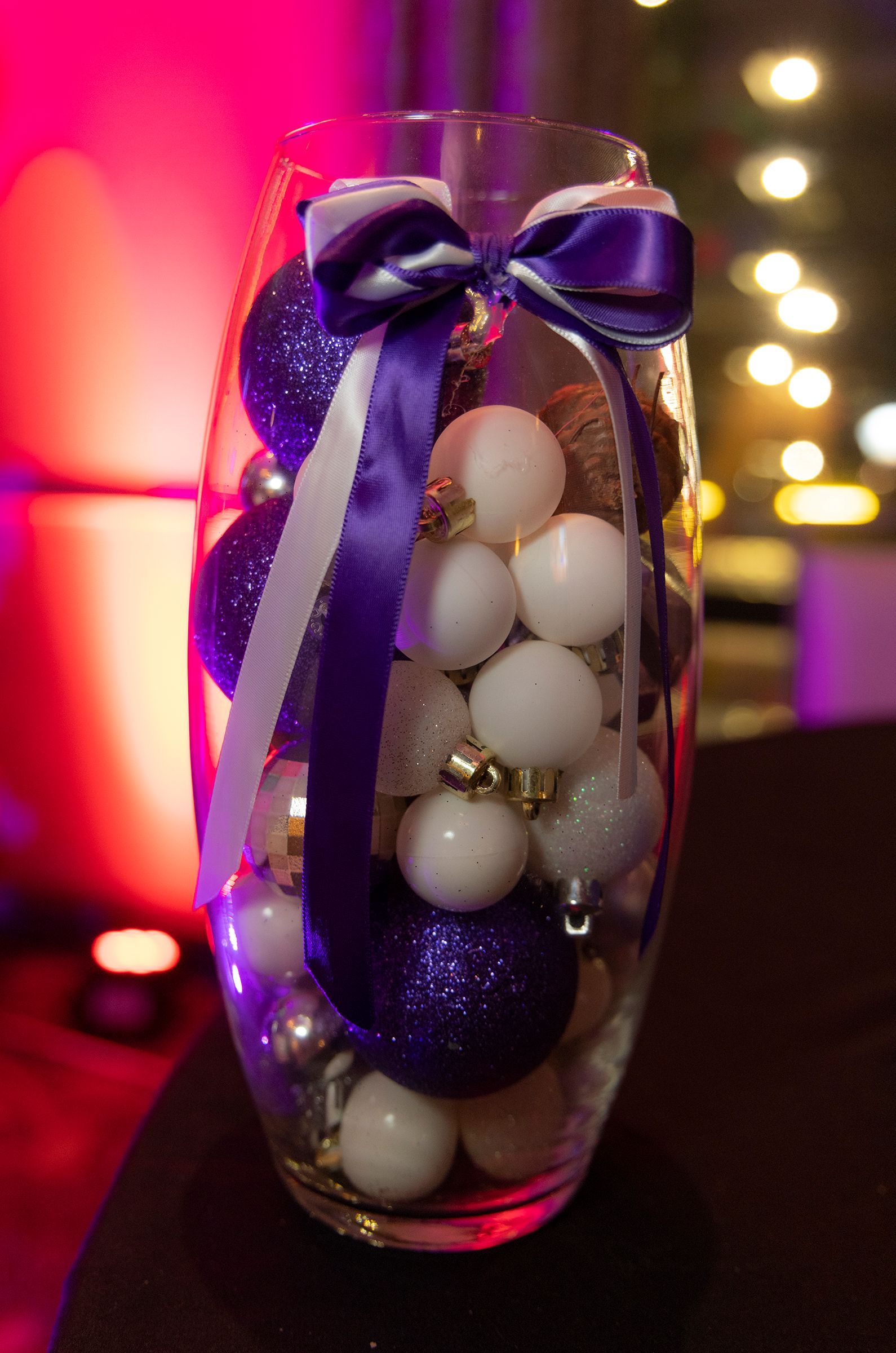 A vase filled with purple and white christmas ornaments and a purple bow.