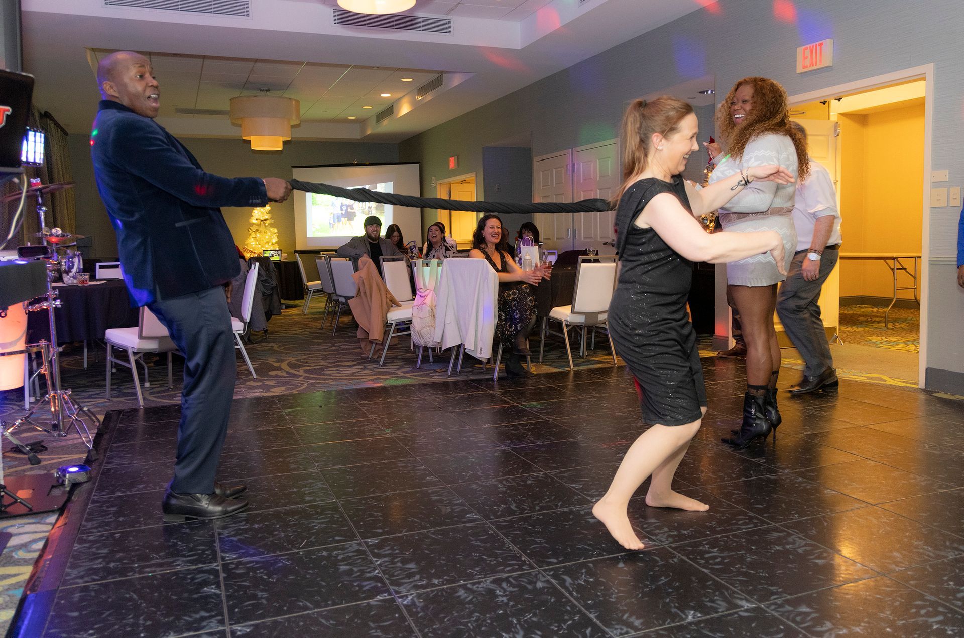 A group of people are dancing in a room with tables and chairs.