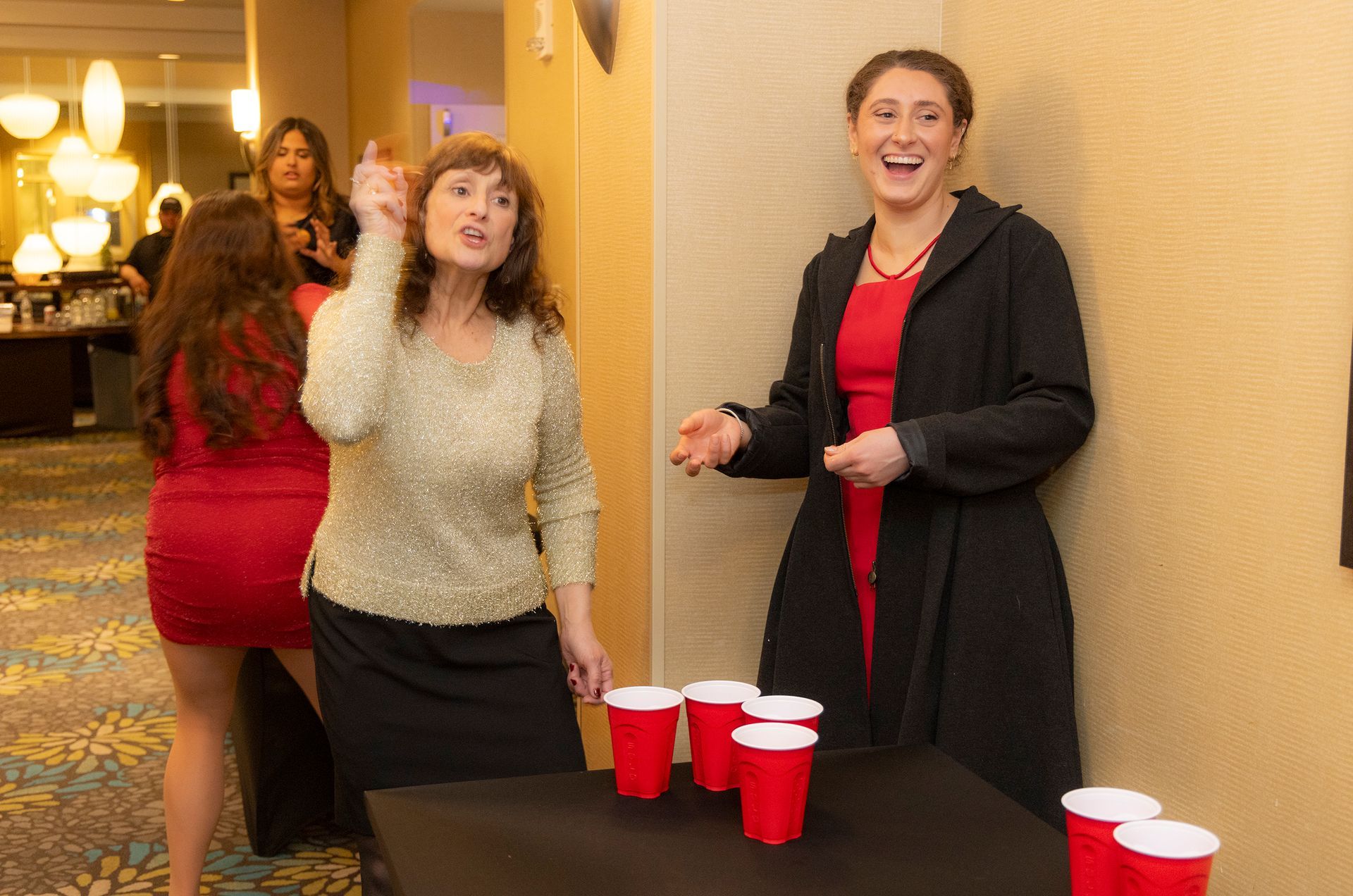 Two women are playing beer pong with red cups on a table.
