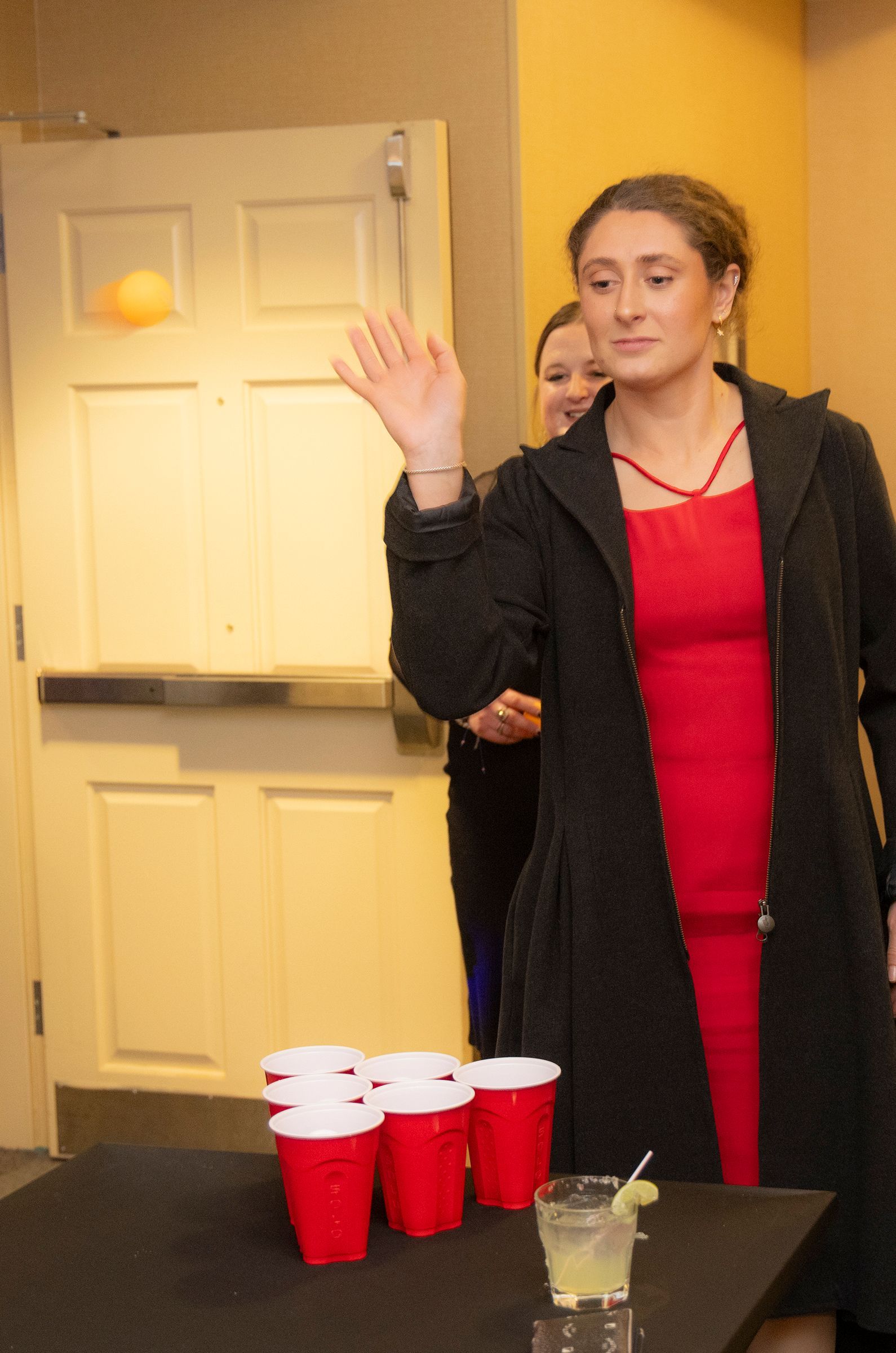 A woman in a red dress is playing beer pong