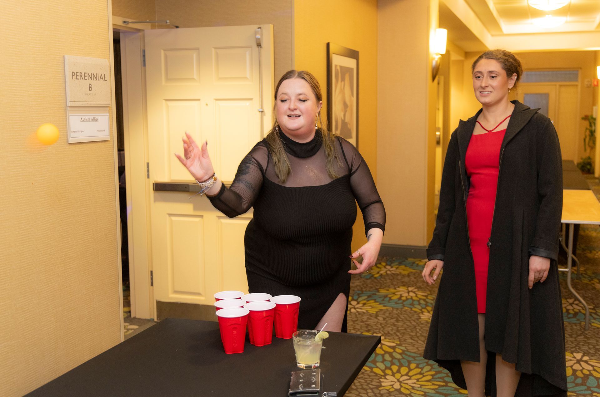 Two women are playing beer pong in a hallway.