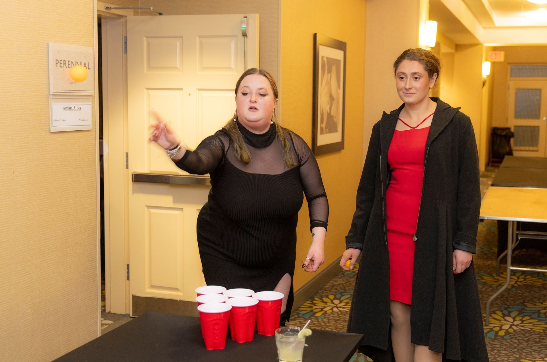 Two women are playing beer pong with red cups on a table.