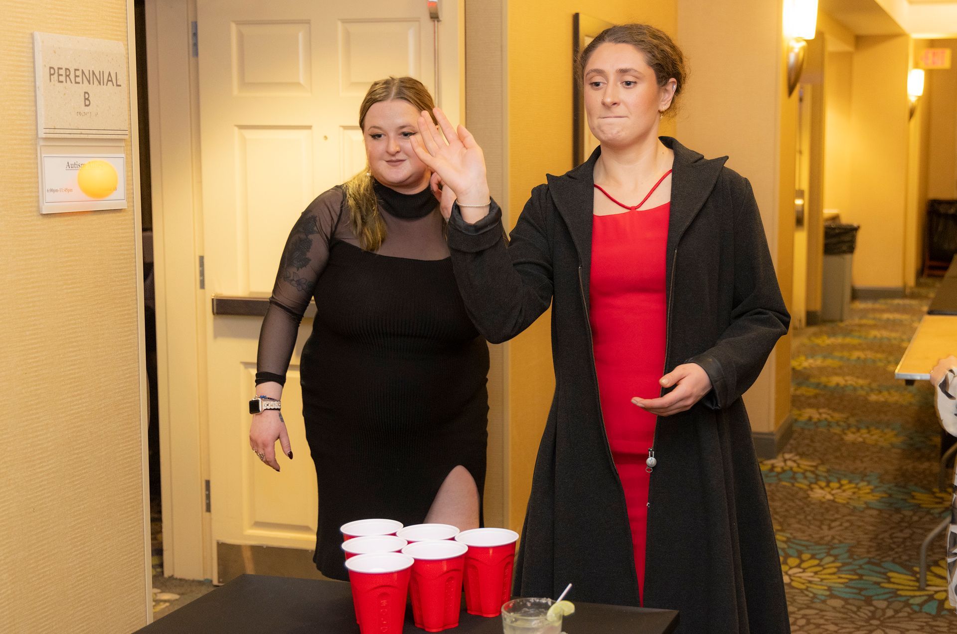 Two women are playing beer pong in a hallway.