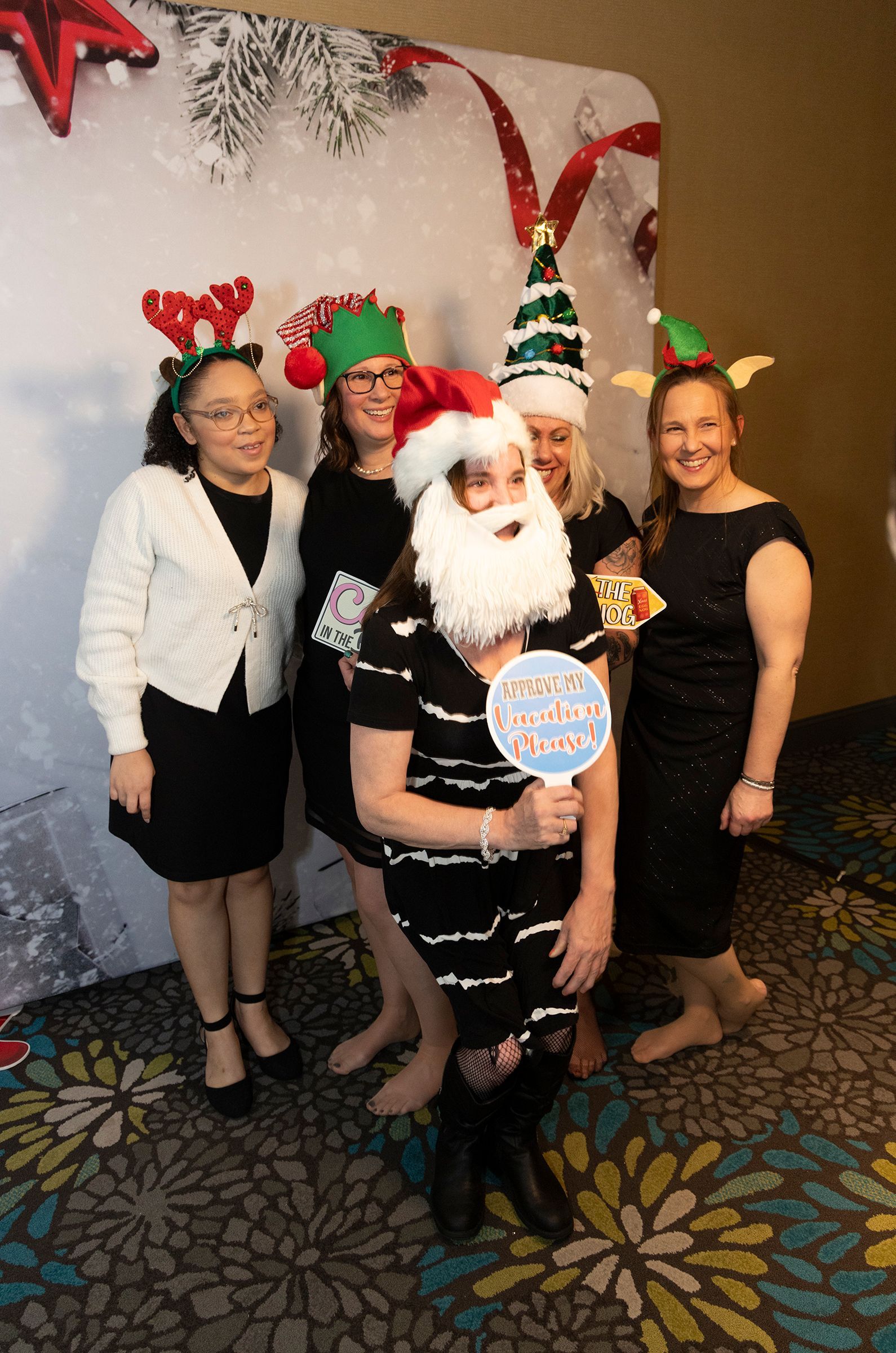 A group of women are posing for a picture in front of a christmas backdrop.