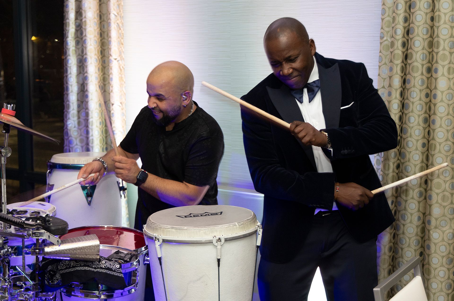 Two men are playing drums in a room.