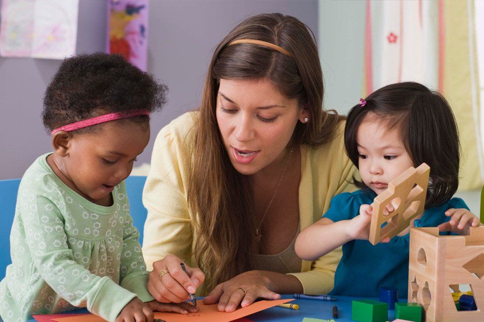 A woman is playing with two little girls at a table.