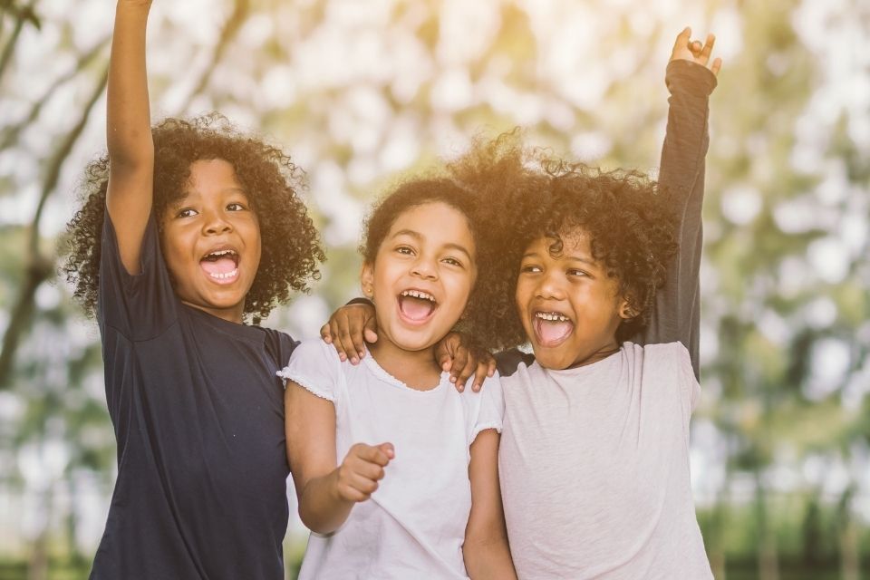 Three young girls are standing next to each other with their arms in the air.
