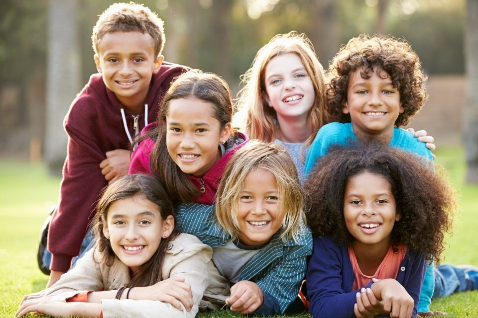 A group of children are laying on top of each other on the grass.