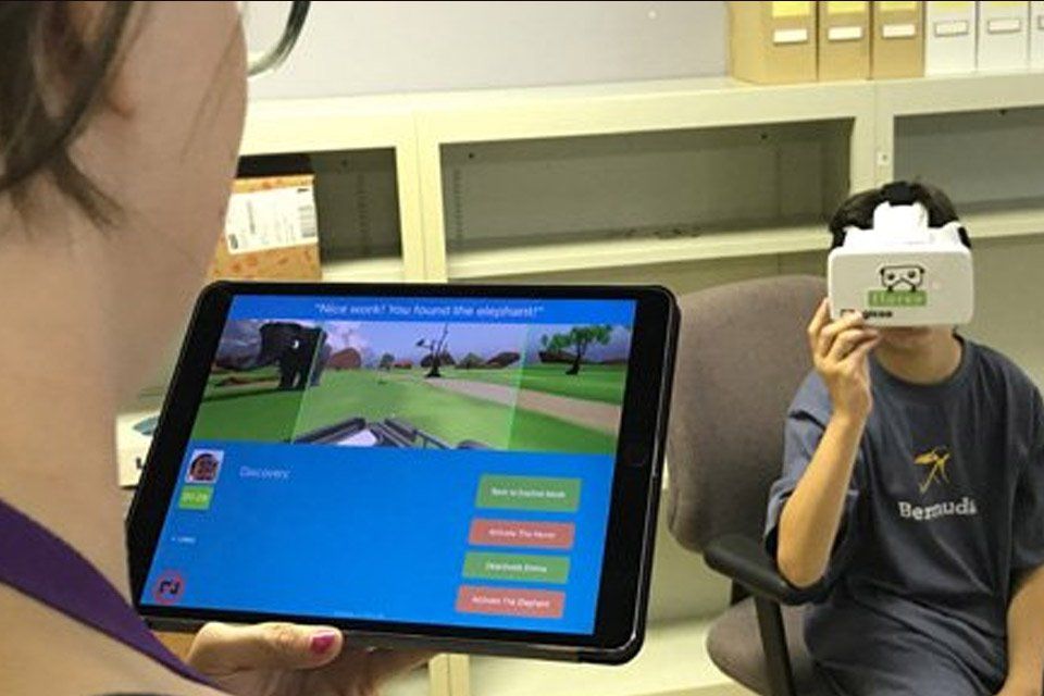 A woman is holding a tablet and a boy is wearing a virtual reality headset.