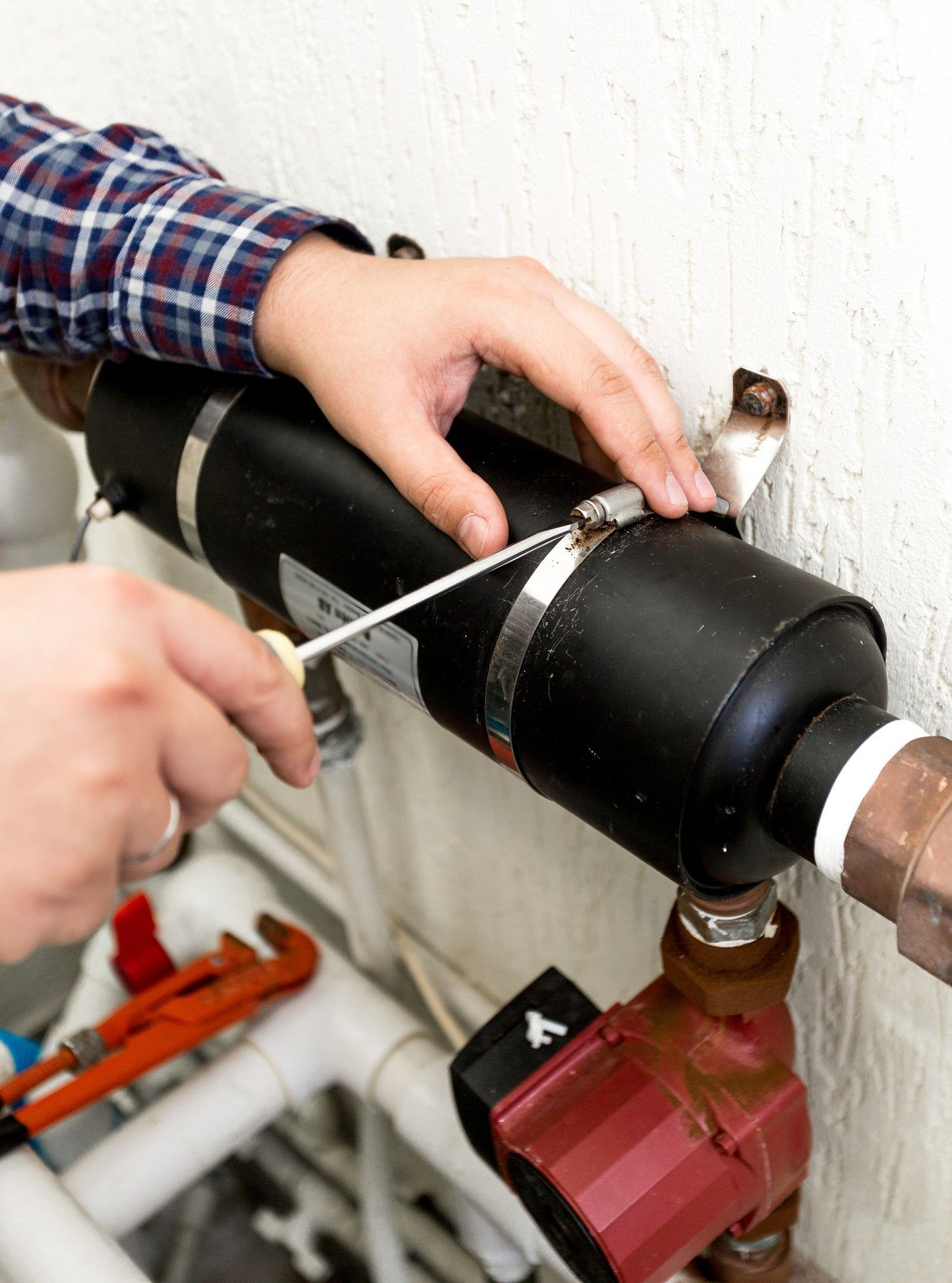 A person is fixing a pipe with a screwdriver.