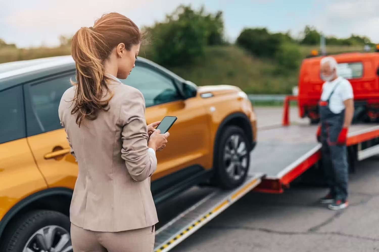 A woman is standing next to a tow truck with a car on it.