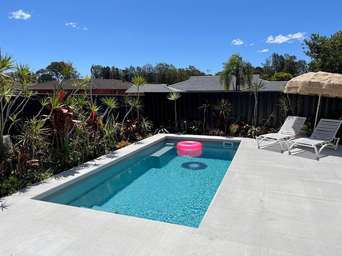 A Small, Blue-tiled Swimming Pool With a Waterfall Feature, Patio, and Glass Fencing — Clearwater Pools Hallidays Point in Hallidays Point, NSW