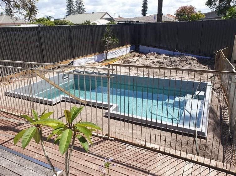L-shaped Swimming Pool Enclosed by a Metal Fence and Wooden Deck — Clearwater Pools Hallidays Point in Pacific Palms, NSW