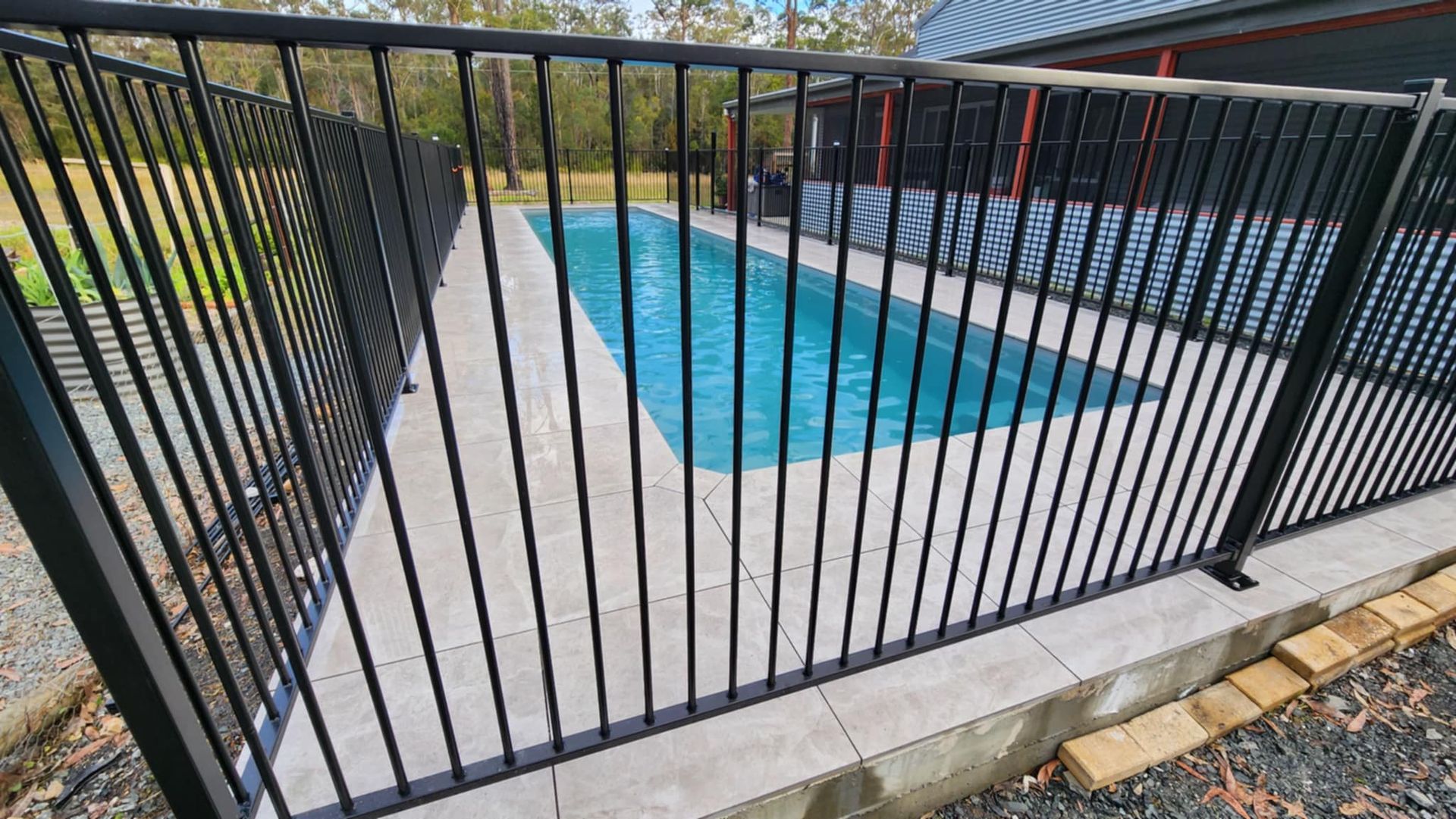 Black Metal Fence Surrounds a Blue Rectangular Pool. Concrete Patio — Clearwater Pools Hallidays Point in Bulahdelah, NSW
