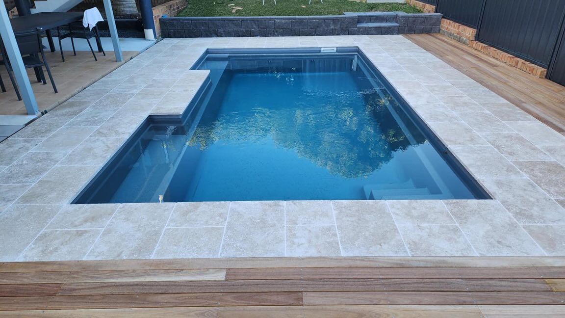 Rectangular pool with light tile surround, set in wooden deck, water reflecting trees. — Clearwater Pools Hallidays Point in Hallidays Point, NSW