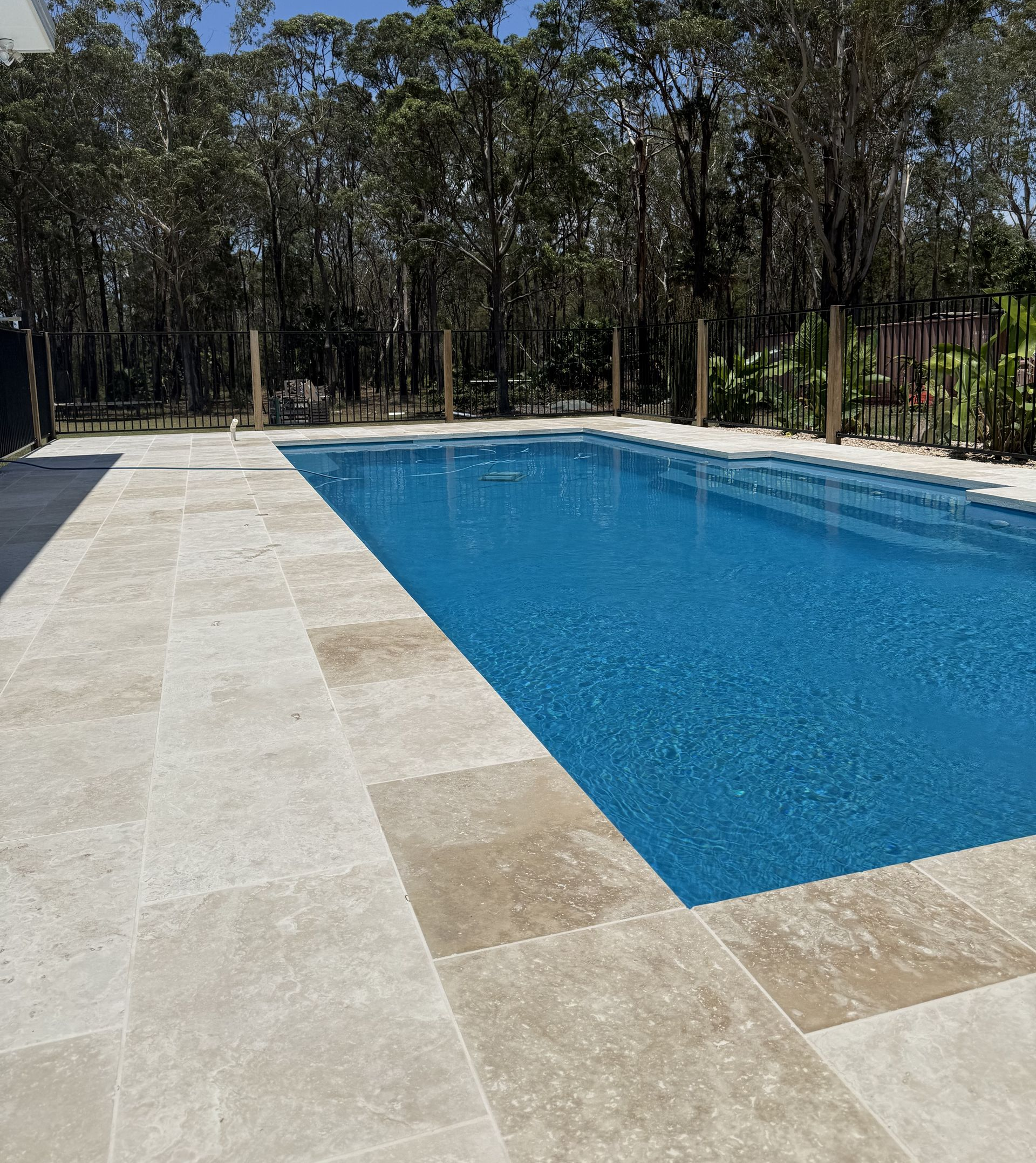 A rectangular swimming pool with blue water, surrounded by light-colored paving. Trees in the background — Clearwater Pools Hallidays Point in Hallidays Point, NSW
