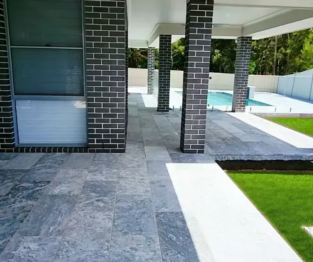 Modern home patio with gray stone flooring, brick columns, and a strip of green lawn