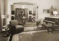 A black and white photo of a living room with a piano and chairs.