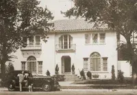 A black and white photo of a house with a car parked in front of it.