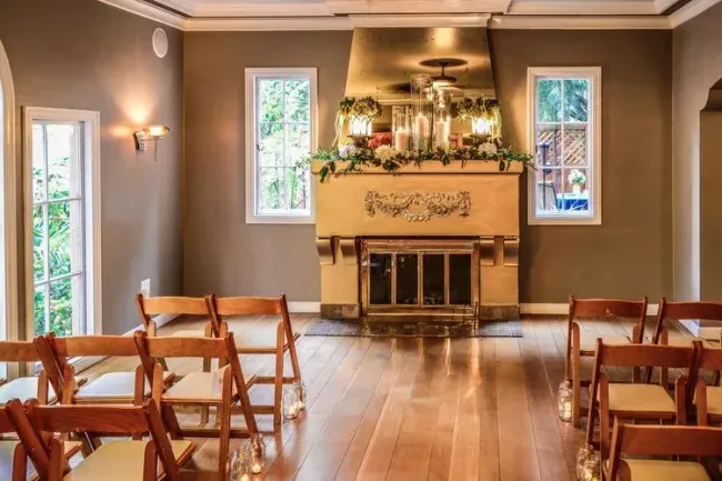 A room with a fireplace and chairs set up for a wedding ceremony.