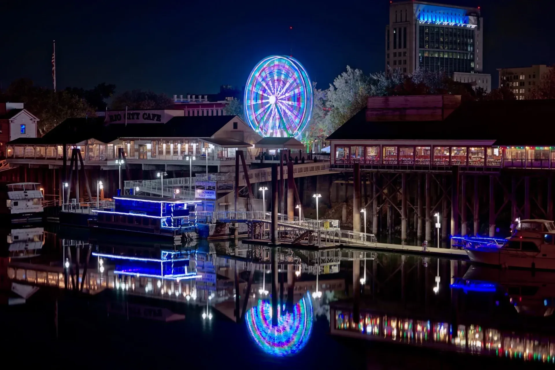 a ferris wheel is lit up at night and is reflected in the water