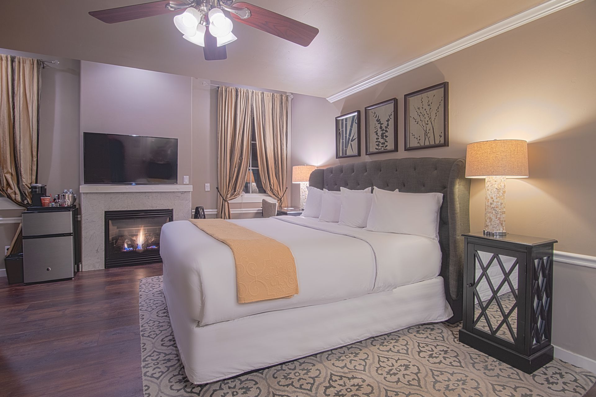 A bedroom with a king size bed , fireplace , television and ceiling fan.