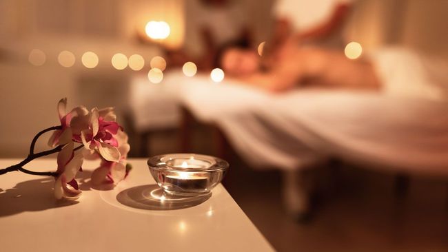 A woman is getting a massage in a spa with a candle and flowers on the table.