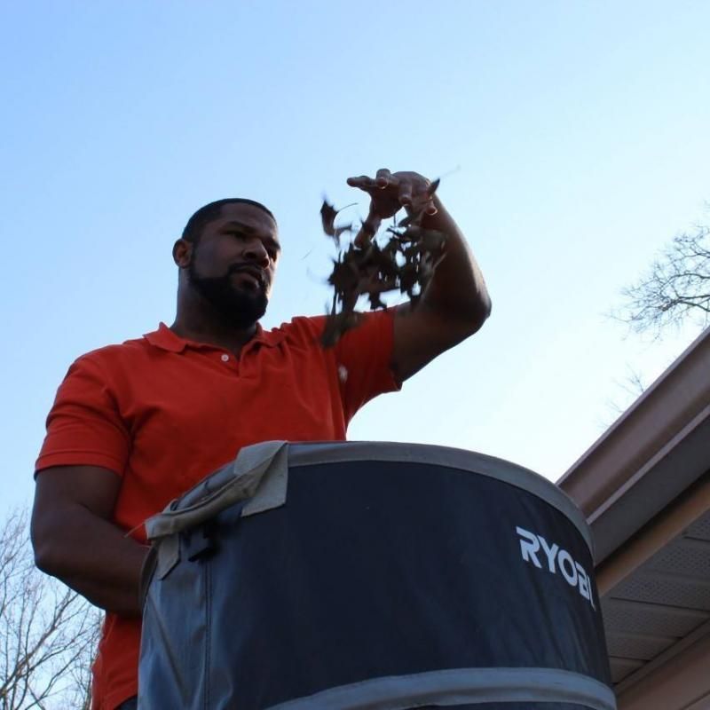 Man in orange shirt putting leaves into a Ryobi container outdoors.