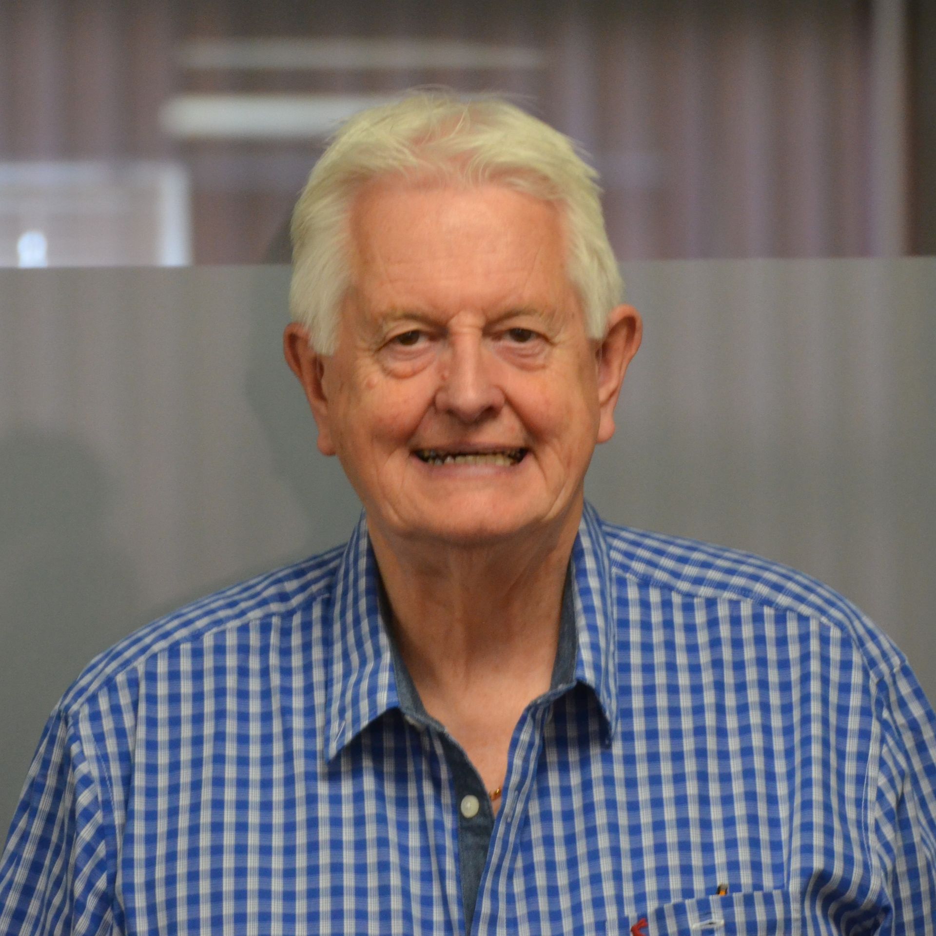 An older man wearing a blue and white checkered shirt is smiling for the camera.