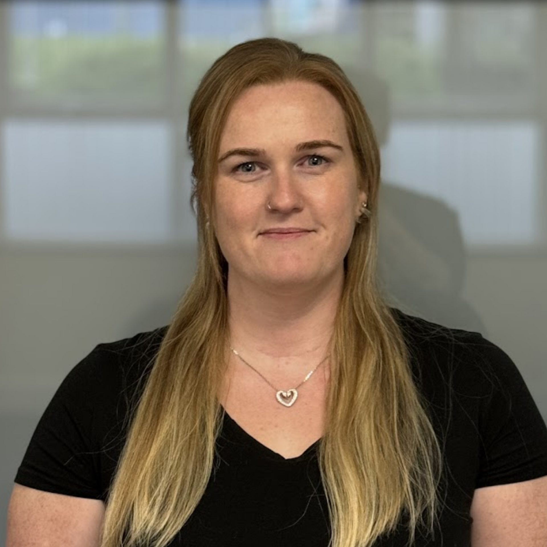 A woman wearing a black shirt and a heart necklace is smiling for the camera.