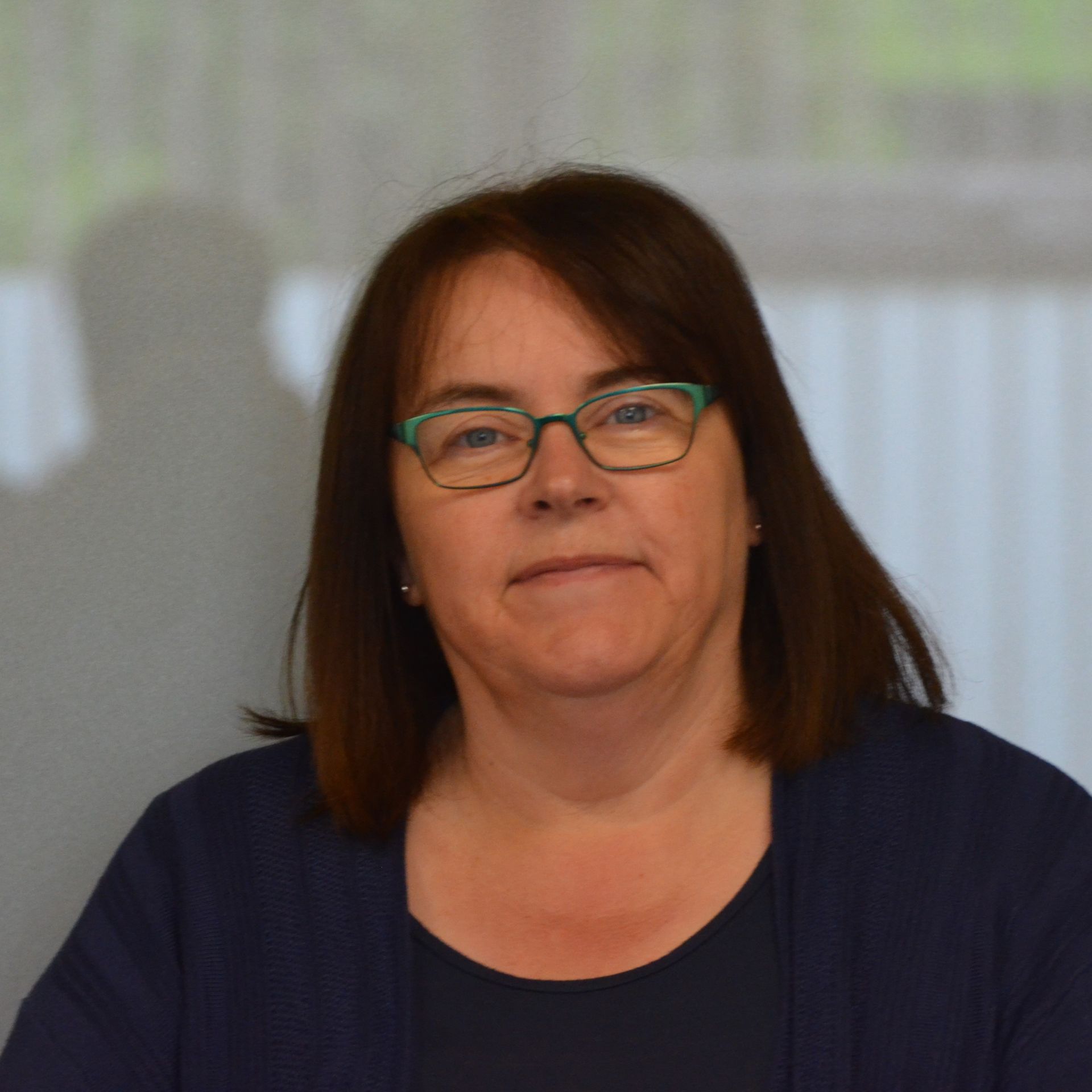 A woman wearing glasses and a blue shirt looks at the camera