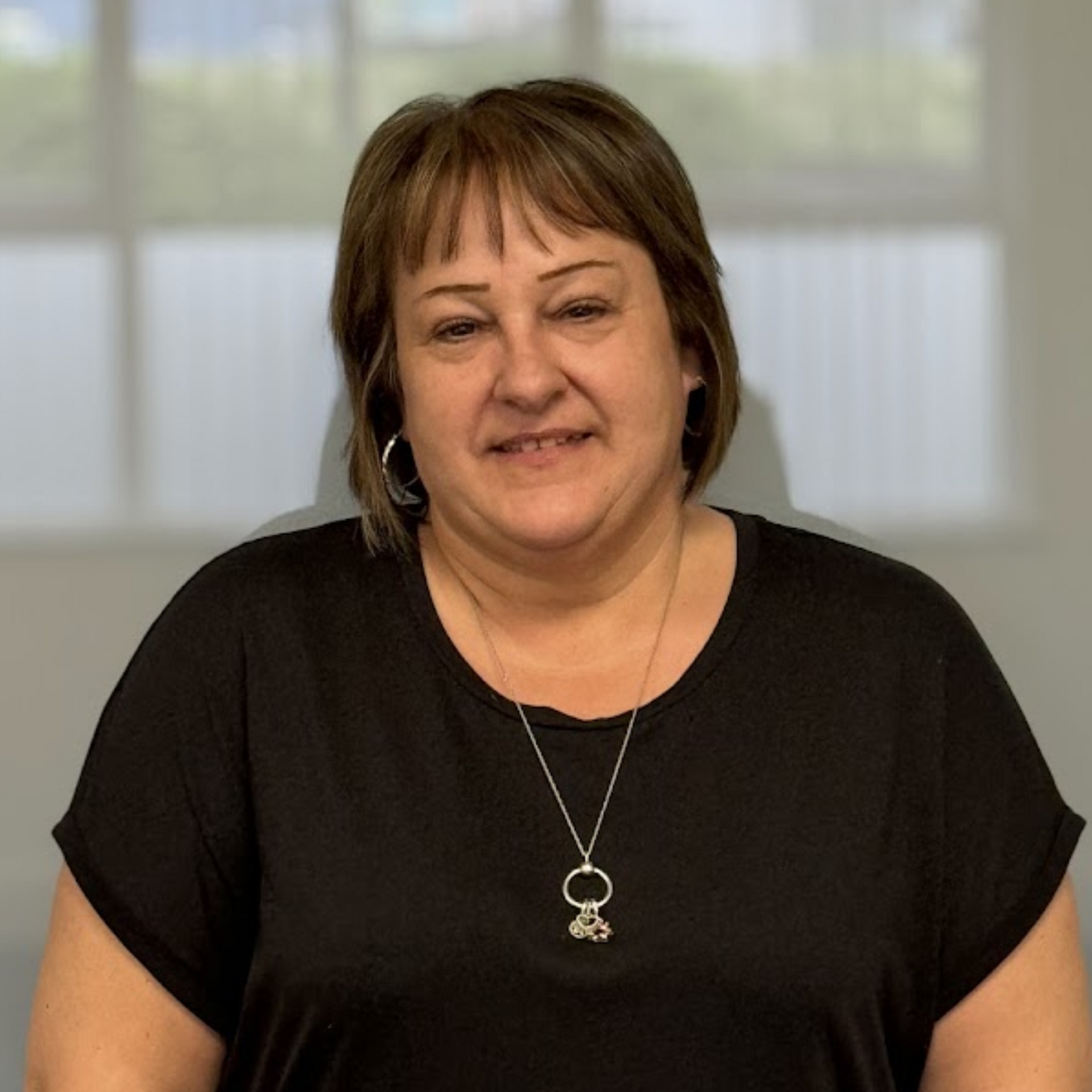 A woman wearing a black shirt and a silver necklace smiles for the camera