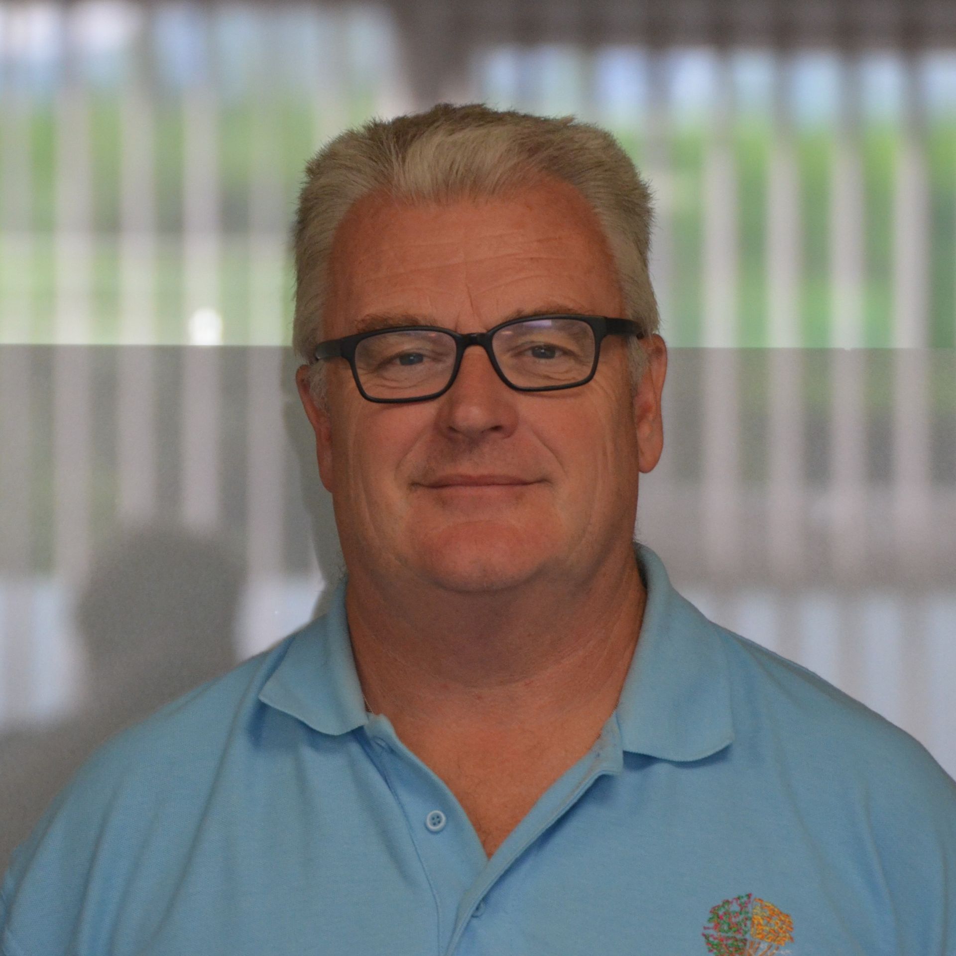 A man wearing glasses and a blue shirt is smiling for the camera