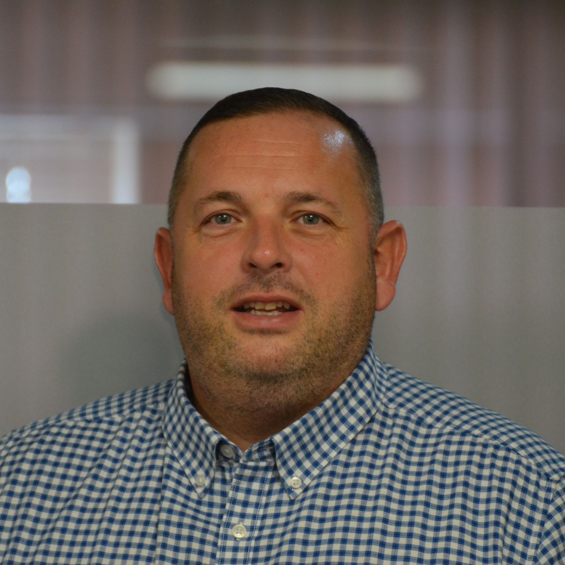 A man in a blue and white checkered shirt is smiling for the camera.